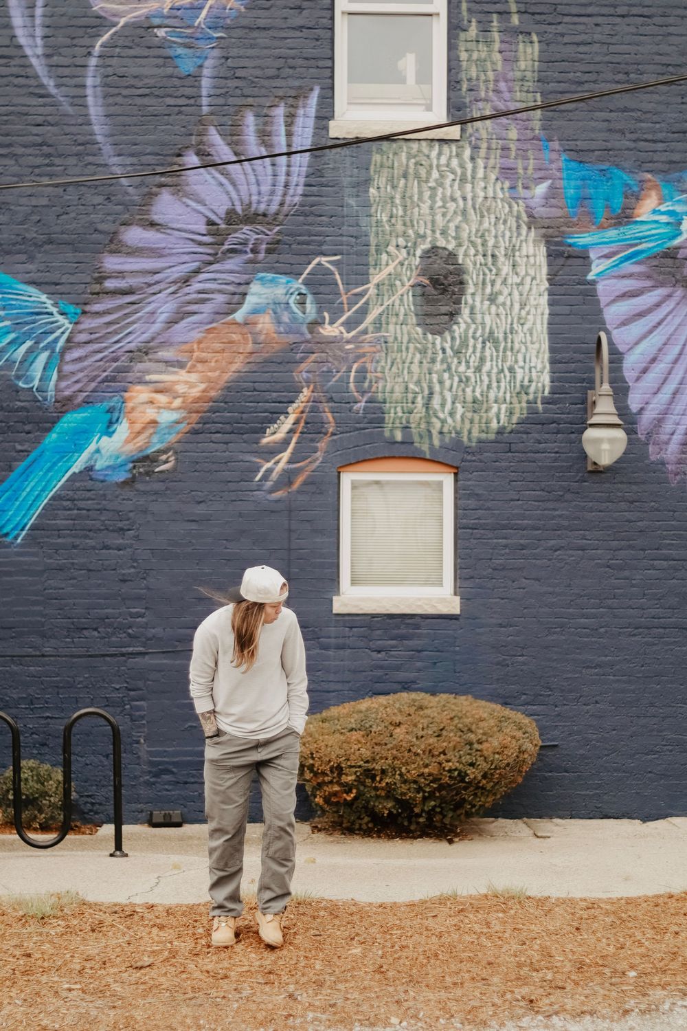 A woman standing against a blue brick wall with bird murals.