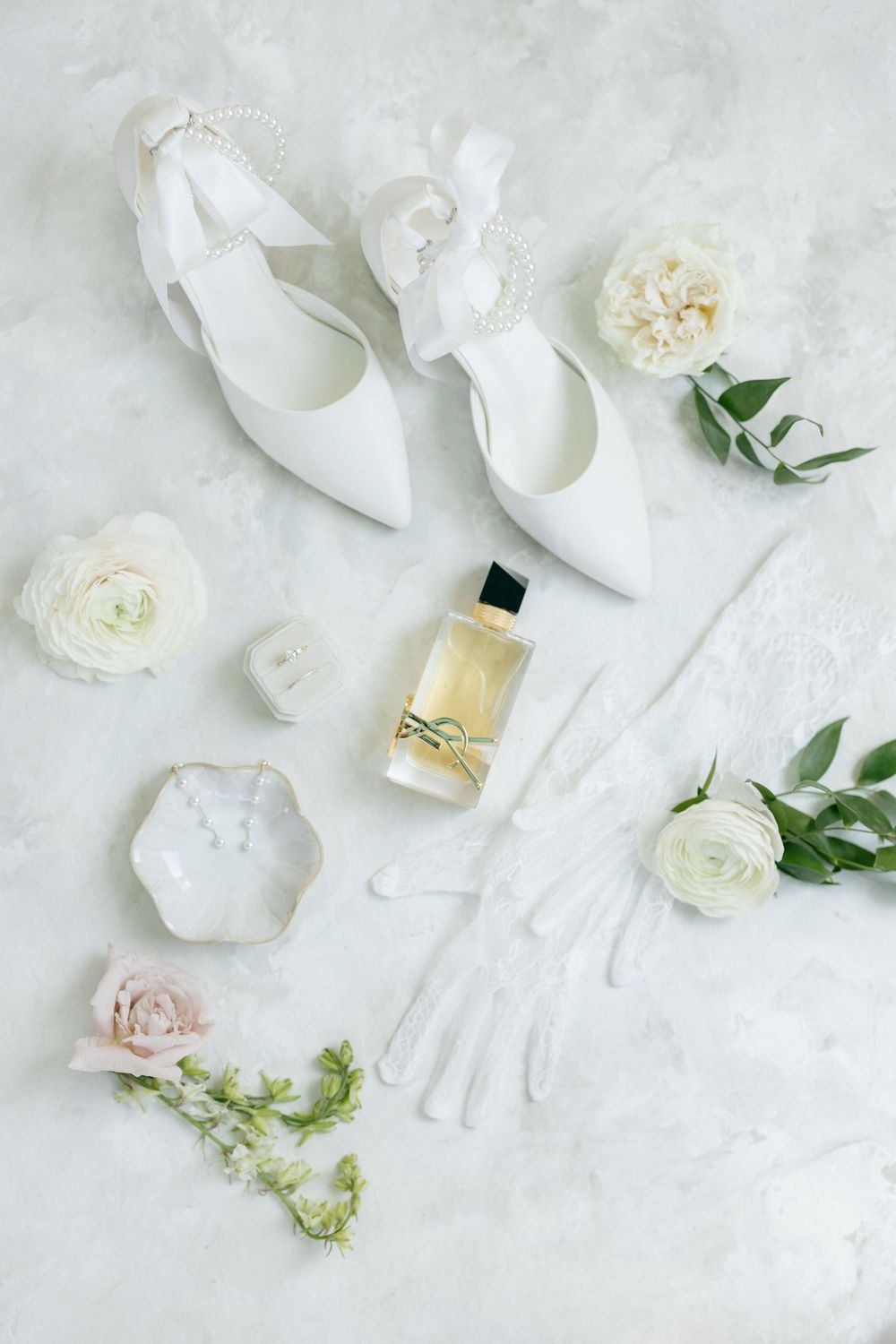 White bridal accessories including shoes, gloves, and delicate flowers arranged on a light background.