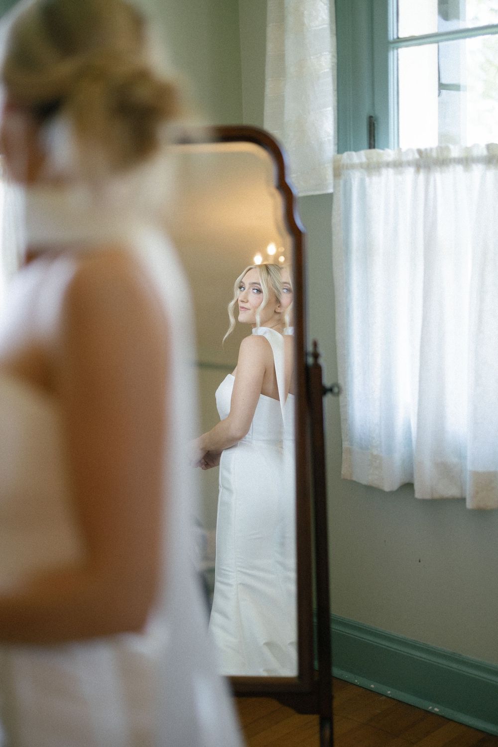 A bride getting ready in a sunlit room with sheer white curtains and elegant decor.