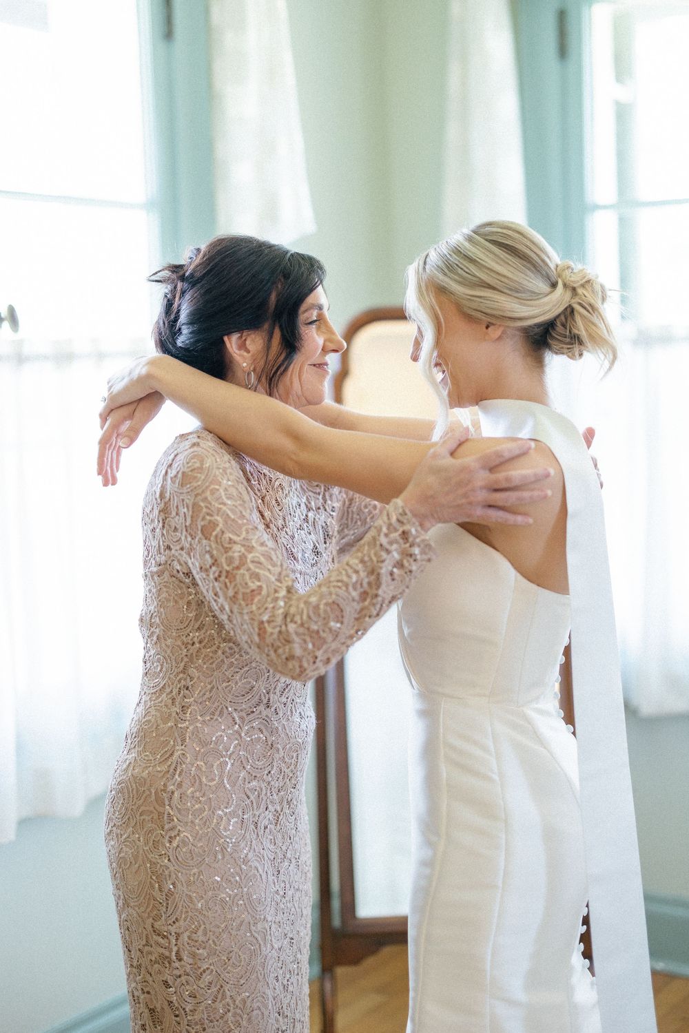 Bridesmaids in blush lace dresses helping the bride prepare for her wedding day.
