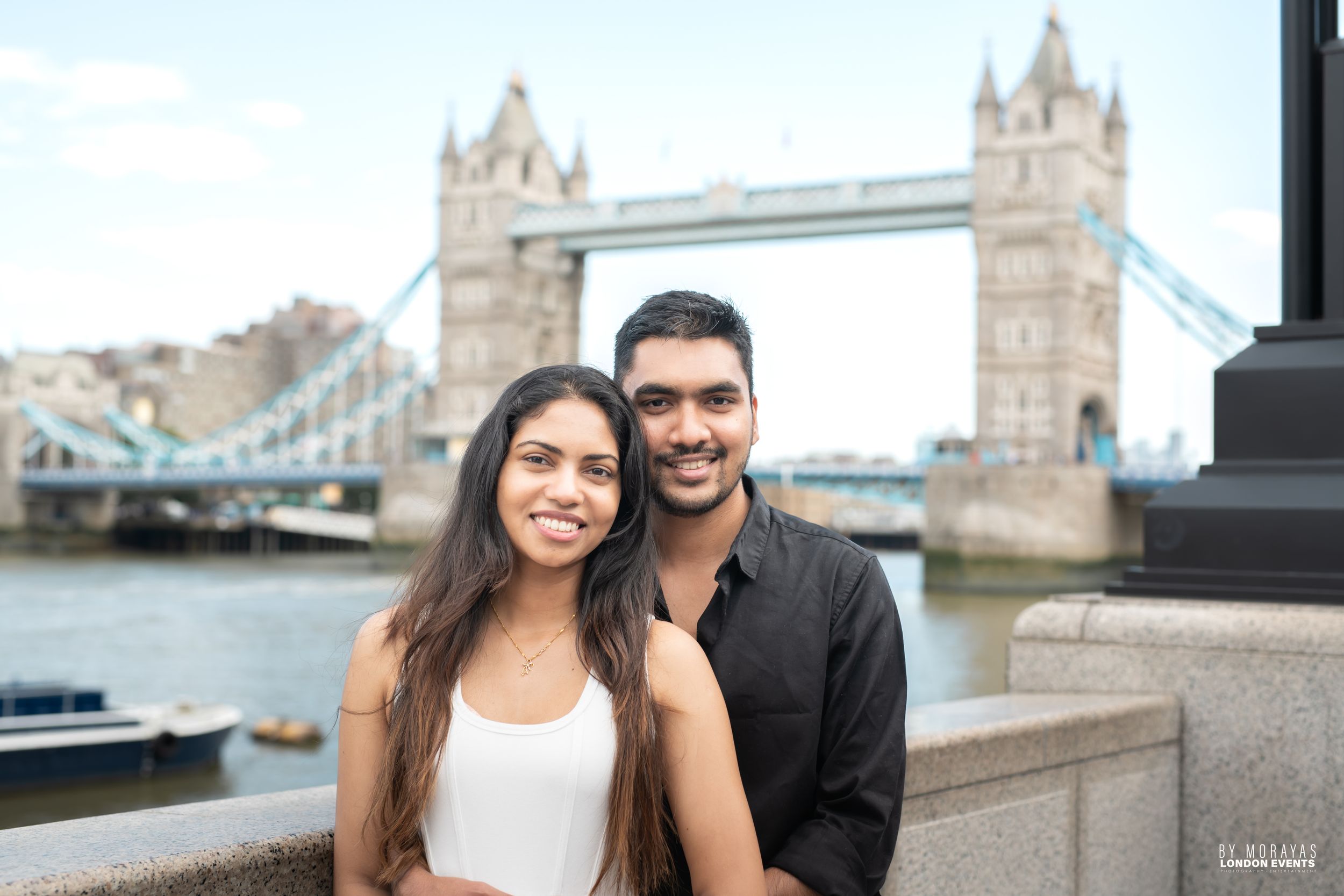 A couple shares an intimate moment near Tower Bridge in London on a sunny day.