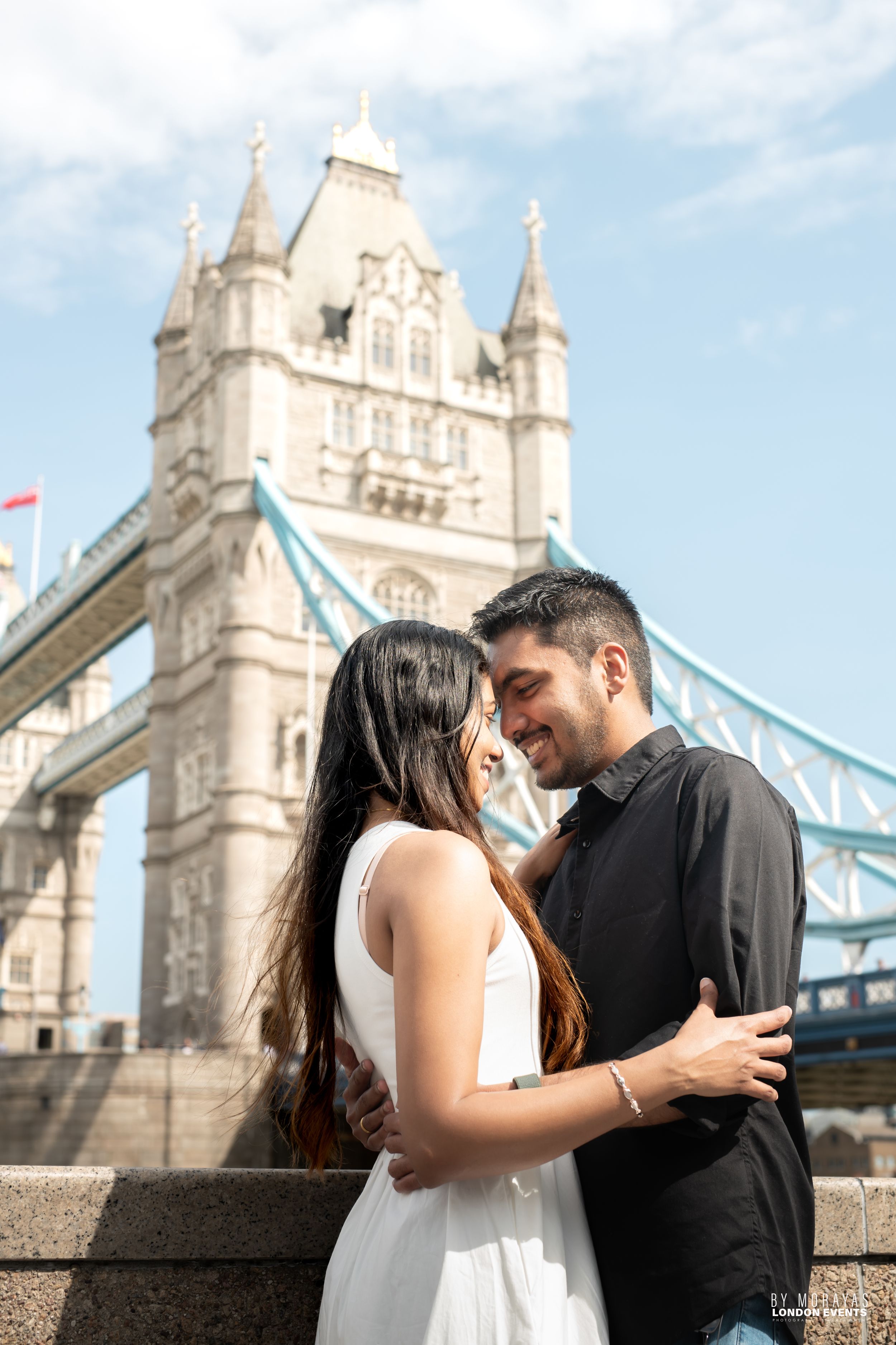 A couple embraces near Tower Bridge in London during a sunny afternoon photoshoot.