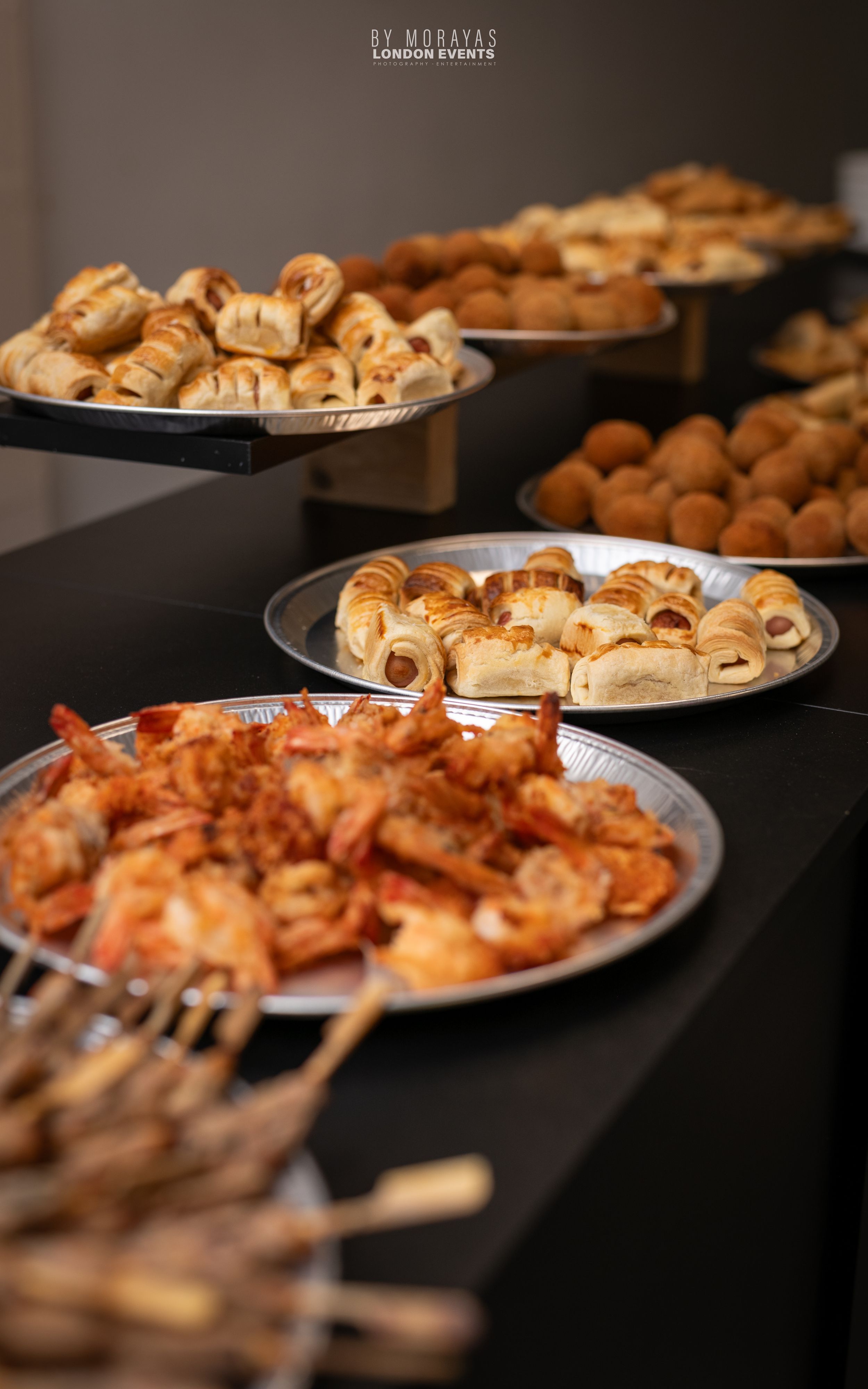 Catering display featuring grilled shrimp and various appetizers on silver platters.