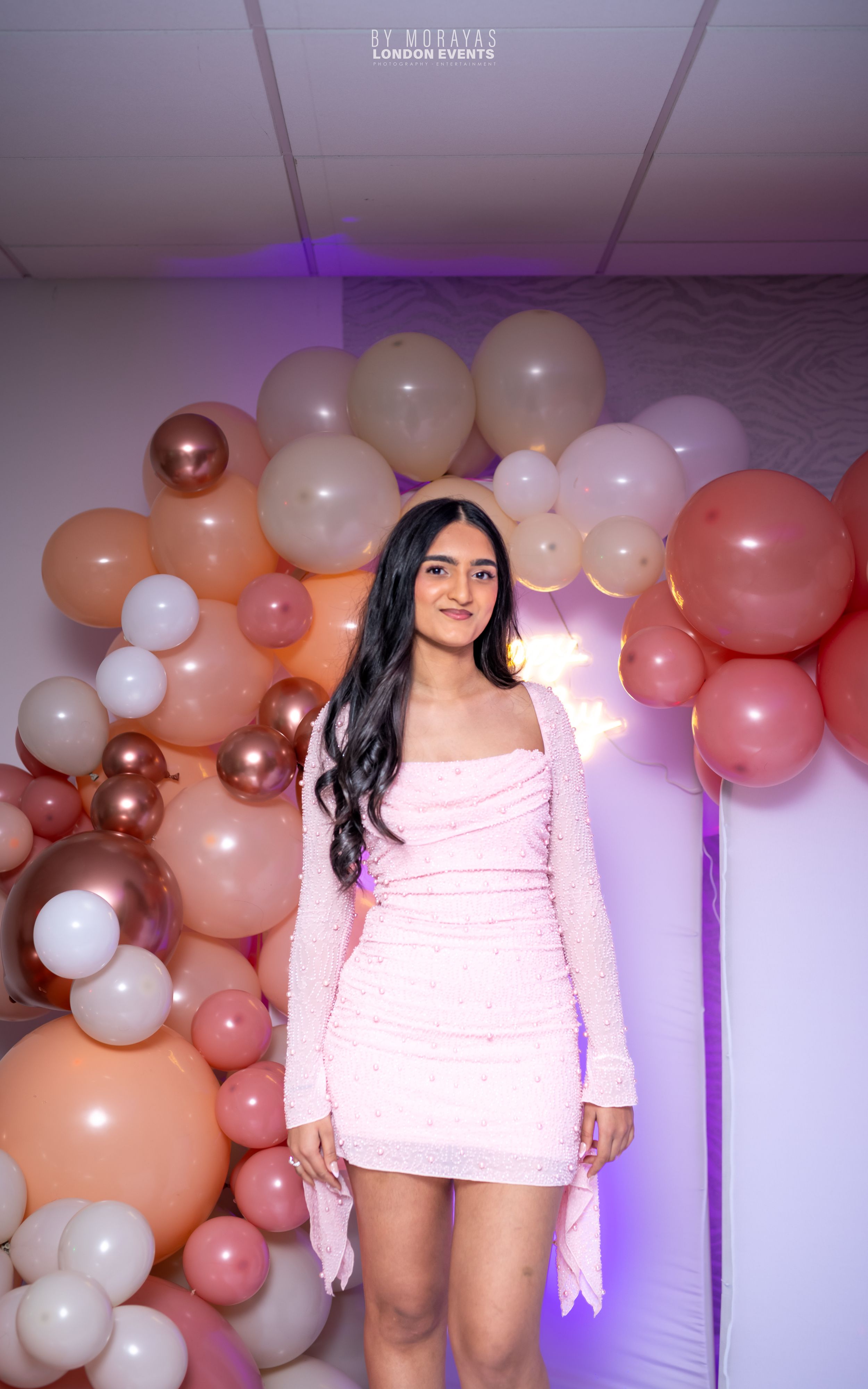 Pink sequin dress against a backdrop of blush and white balloon garland at a celebration event.
