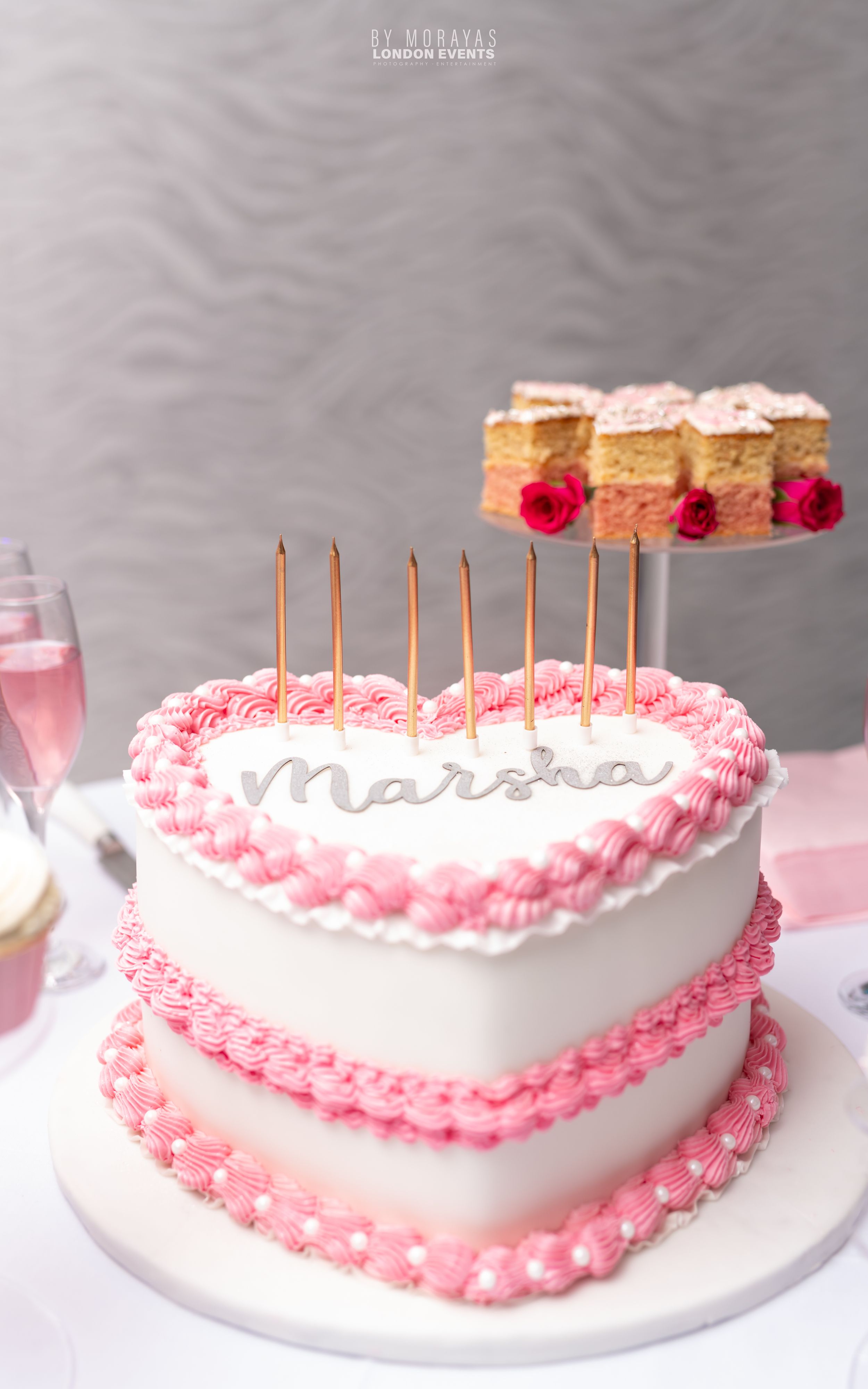 White birthday cake with pink frosting details and candles on a white plate.