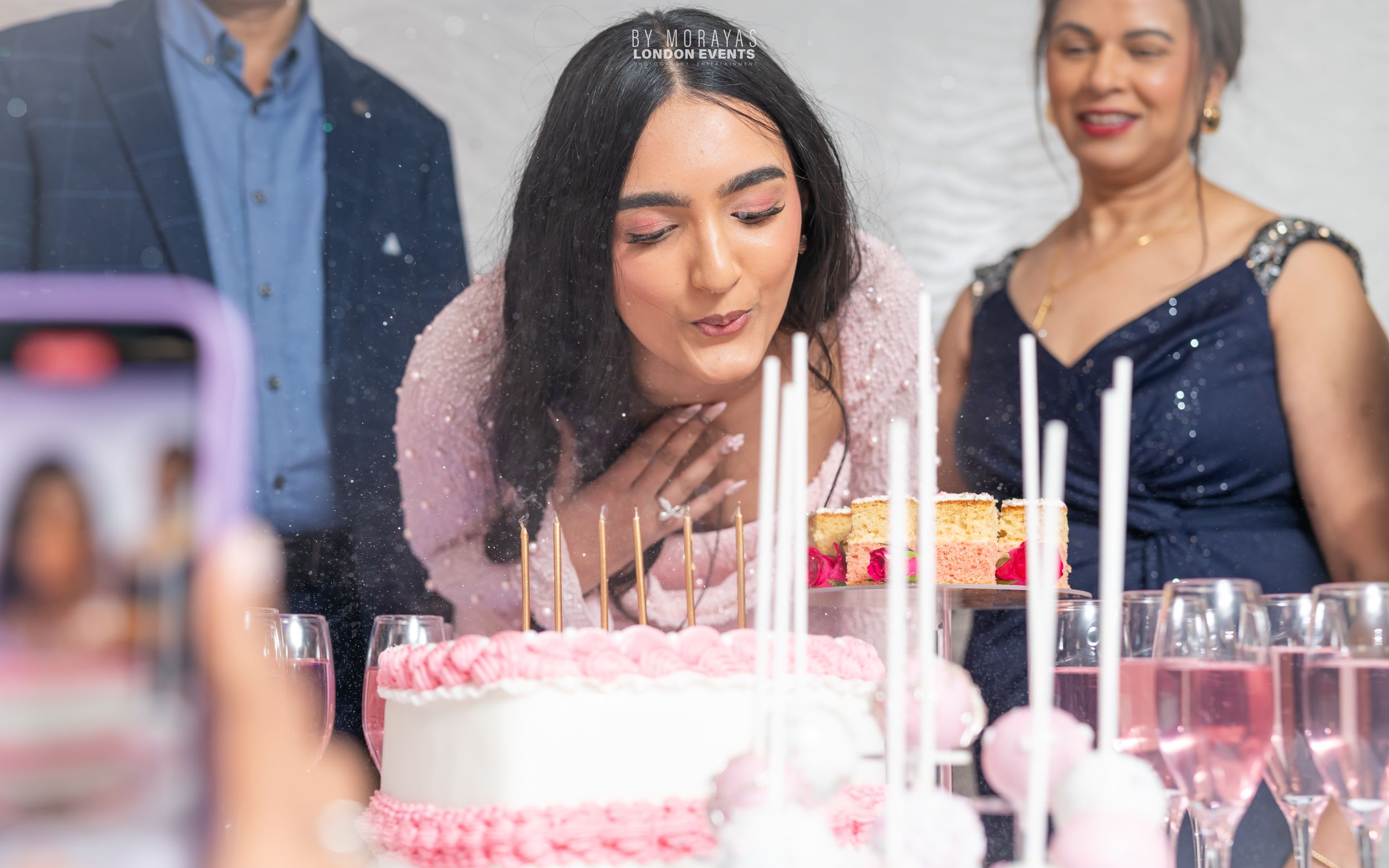 Celebration scene with pink birthday cake and champagne glasses.