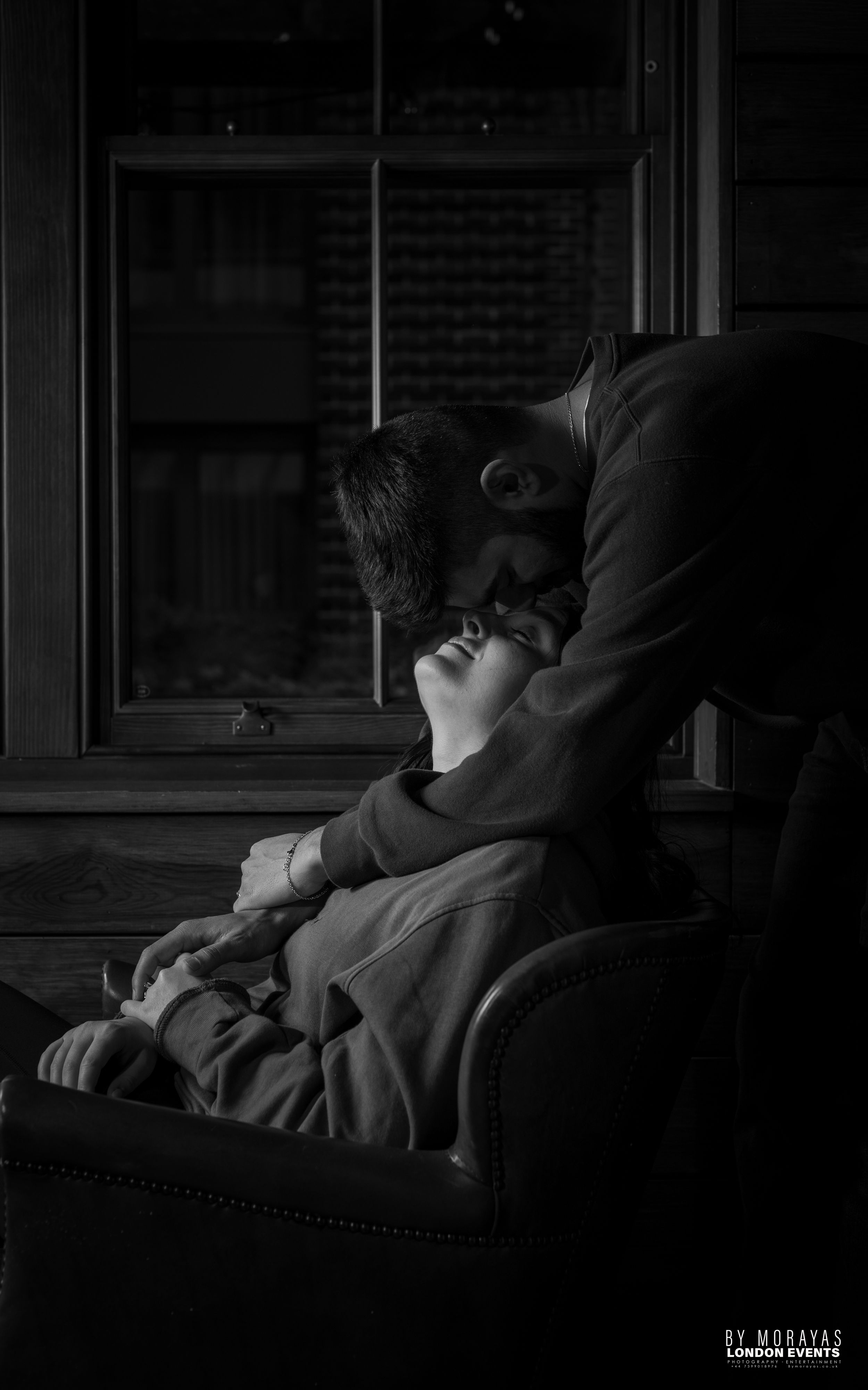 A dimly lit scene shows silhouettes relaxing on a couch in dramatic lighting.