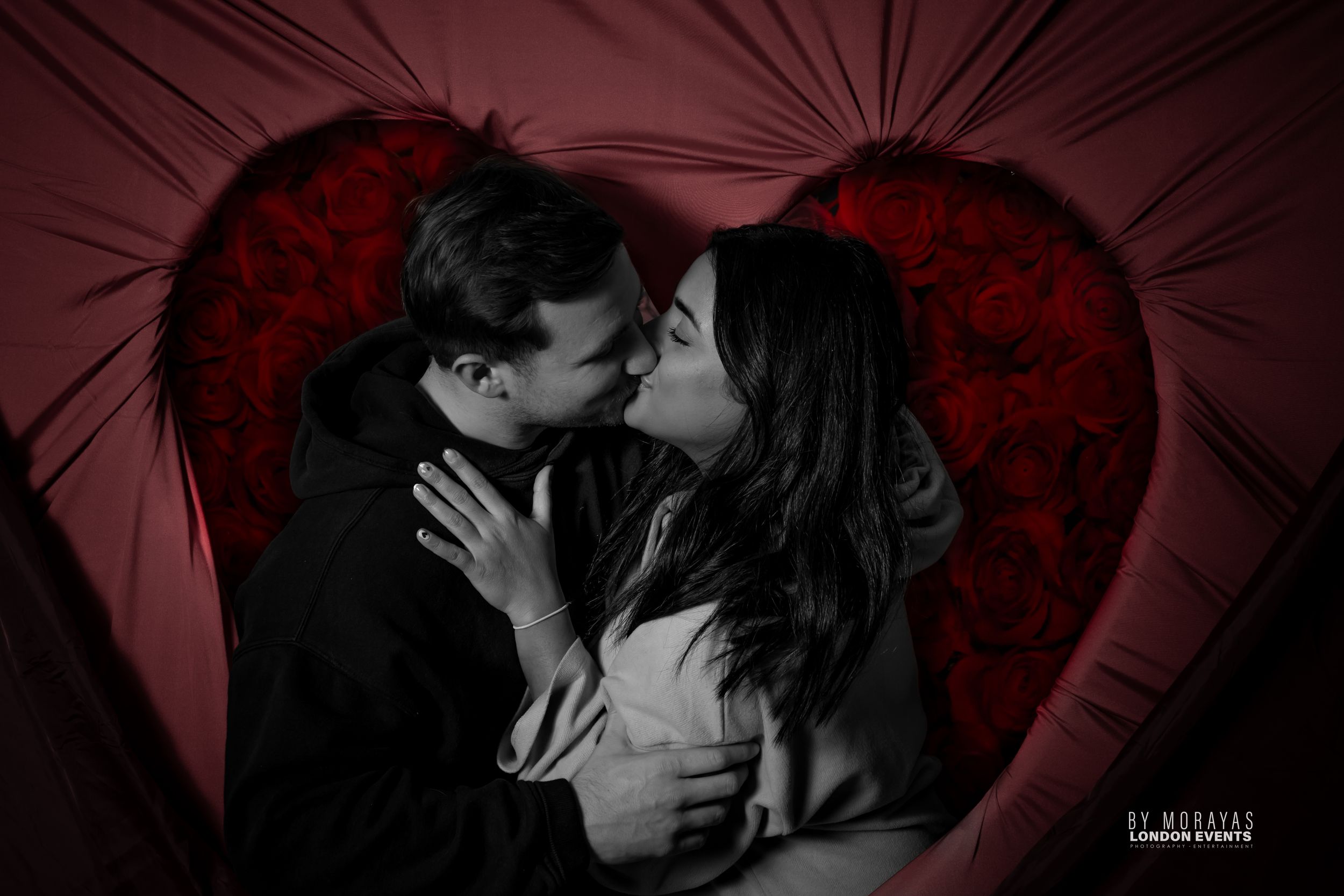 Intimate portrait of couple embracing in front of red heart-shaped backdrop.