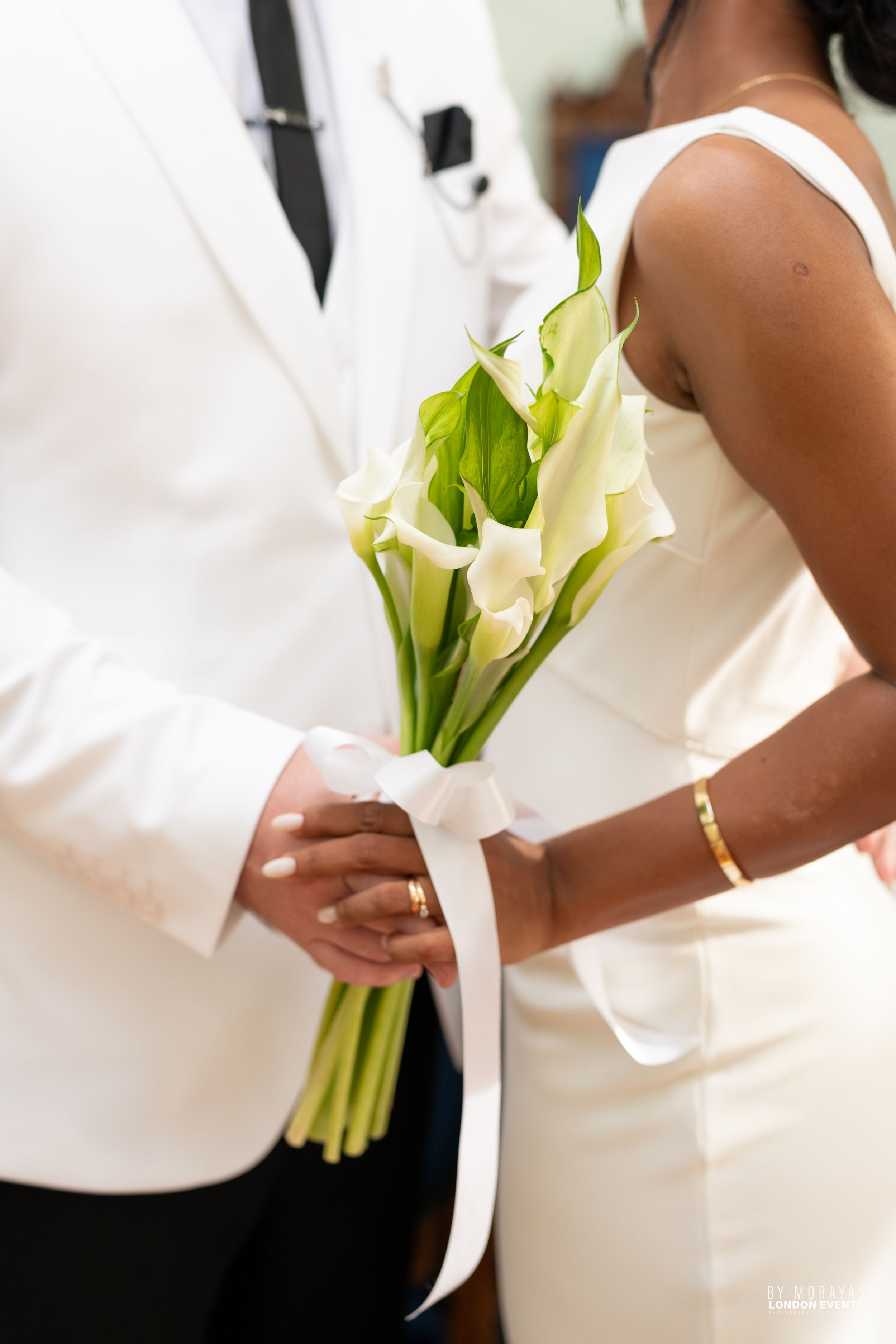 Elegant wedding couple holding white calla lily bouquets in formal attire.