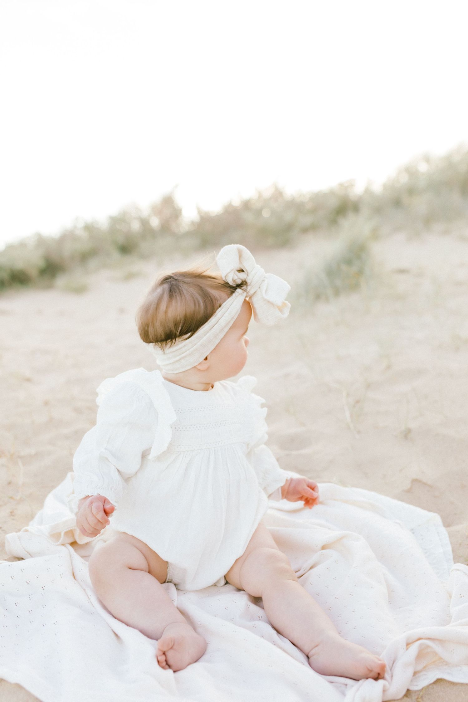 A series of soft, ethereal photos showing someone lying on a white blanket in the sand at the beach.