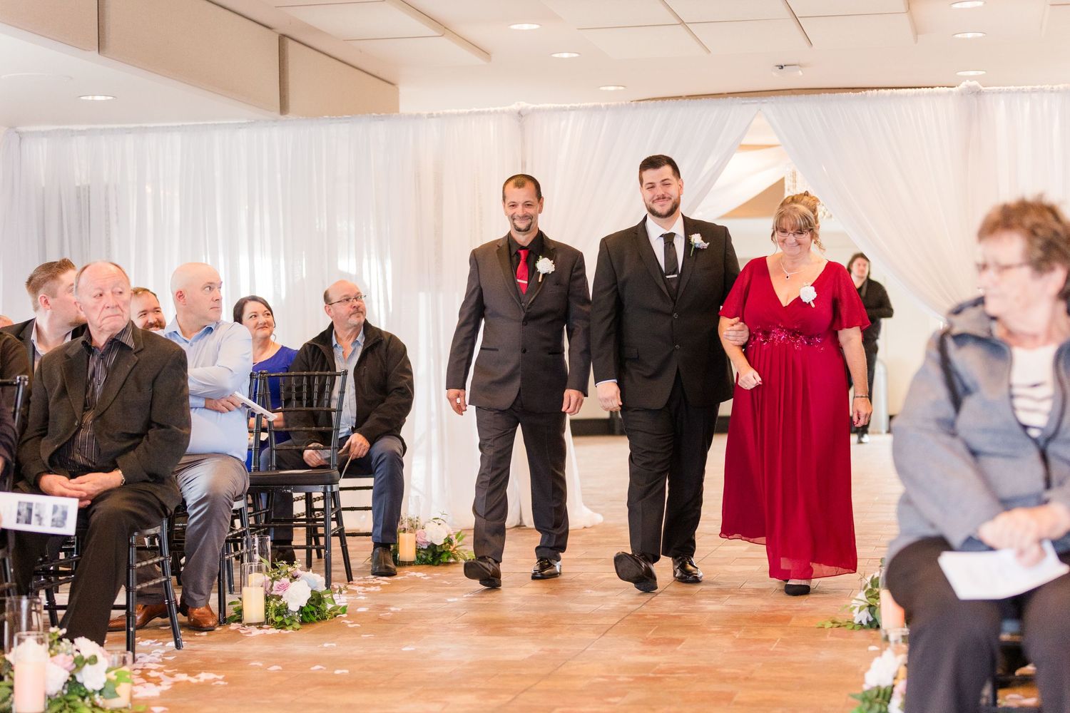 Wedding guests dance and celebrate during a reception in a bright white banquet hall with elegant decor.