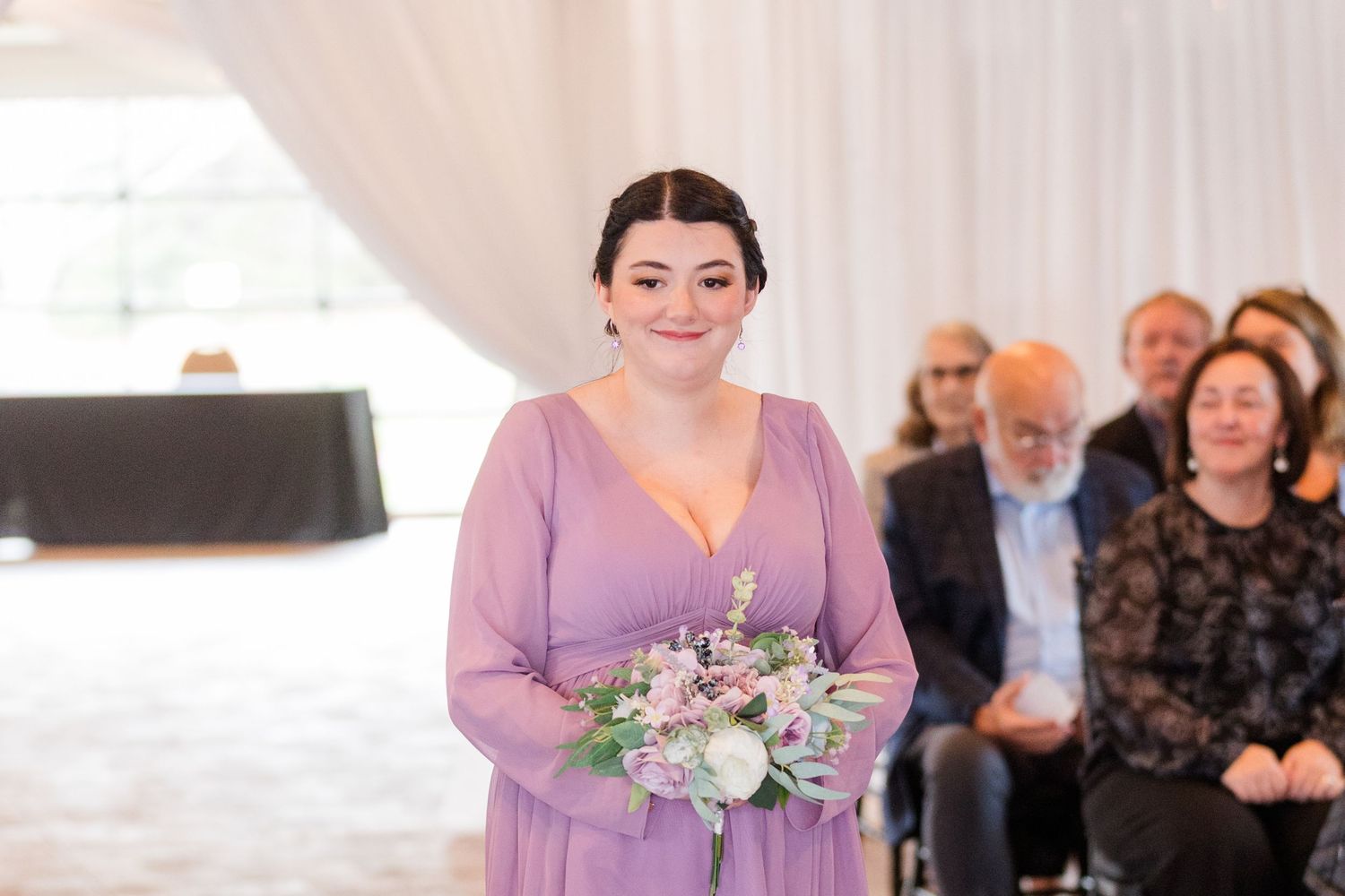 Wedding party members in lavender dresses pose together during an elegant indoor celebration.