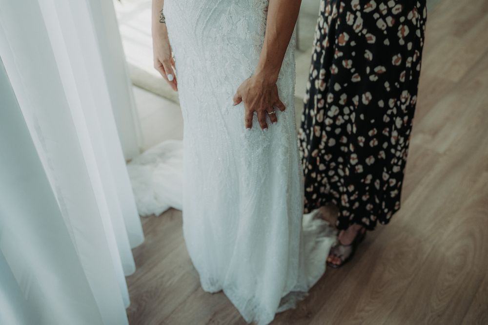 Close-up detail of white lace wedding dress hem against hardwood floor.