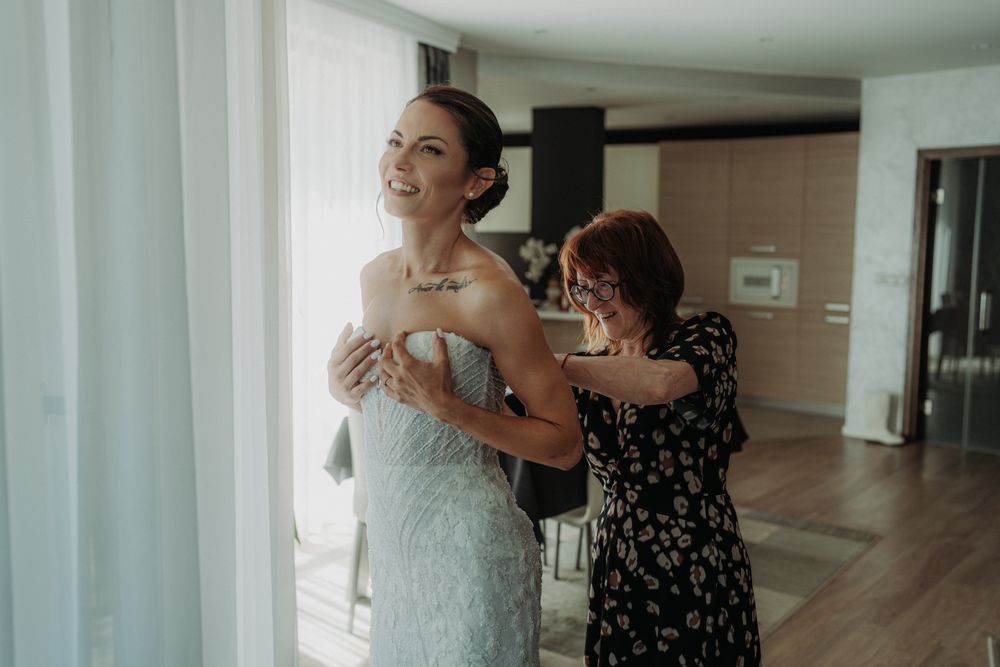 Bridal preparations in a bright modern room with white curtains and natural lighting.