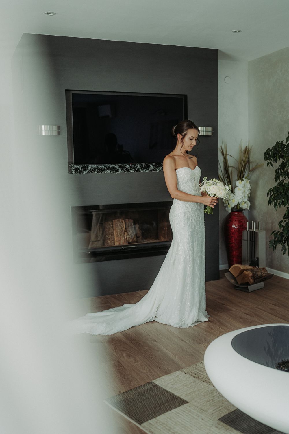 Elegant white wedding dress photographed in a modern interior with wooden floors and dark walls.