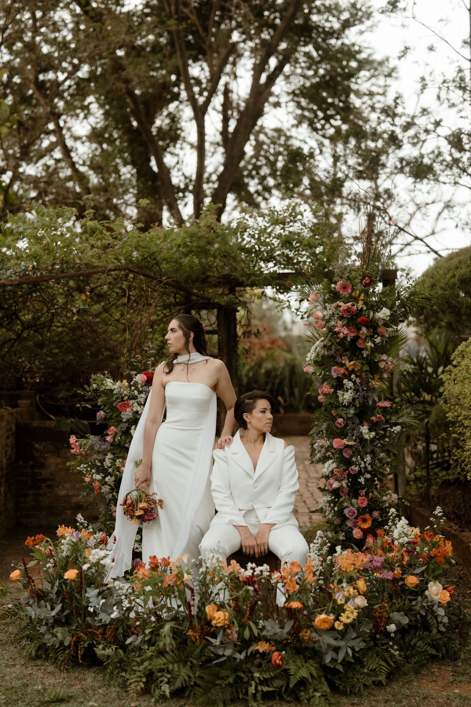 A romantic garden scene with two figures in white attire seated among vibrant roses and autumn-colored flowers.