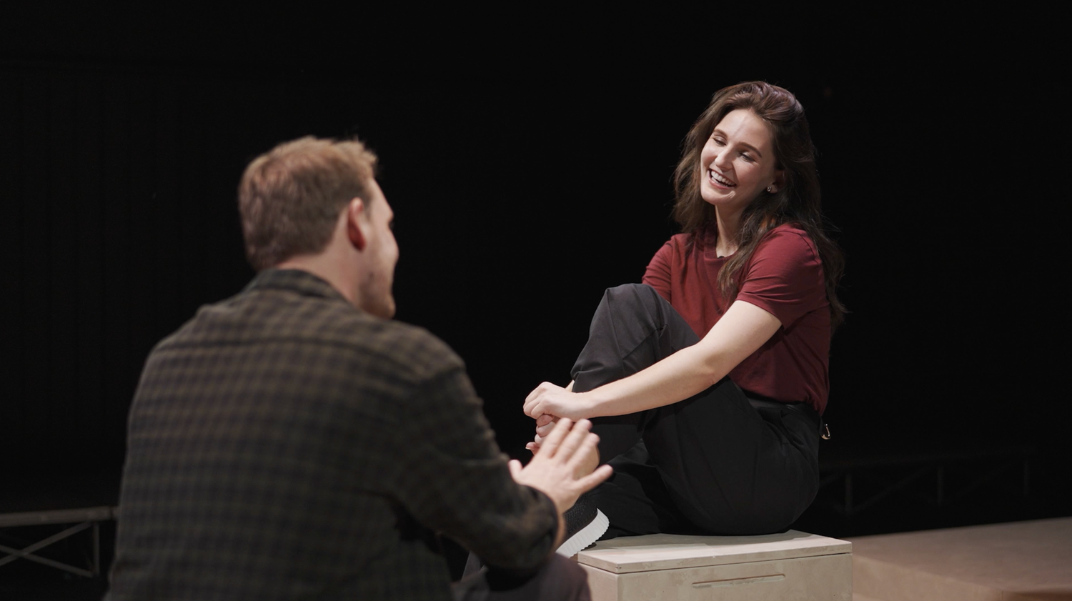 People seated at a dark table engaged in conversation against black background.