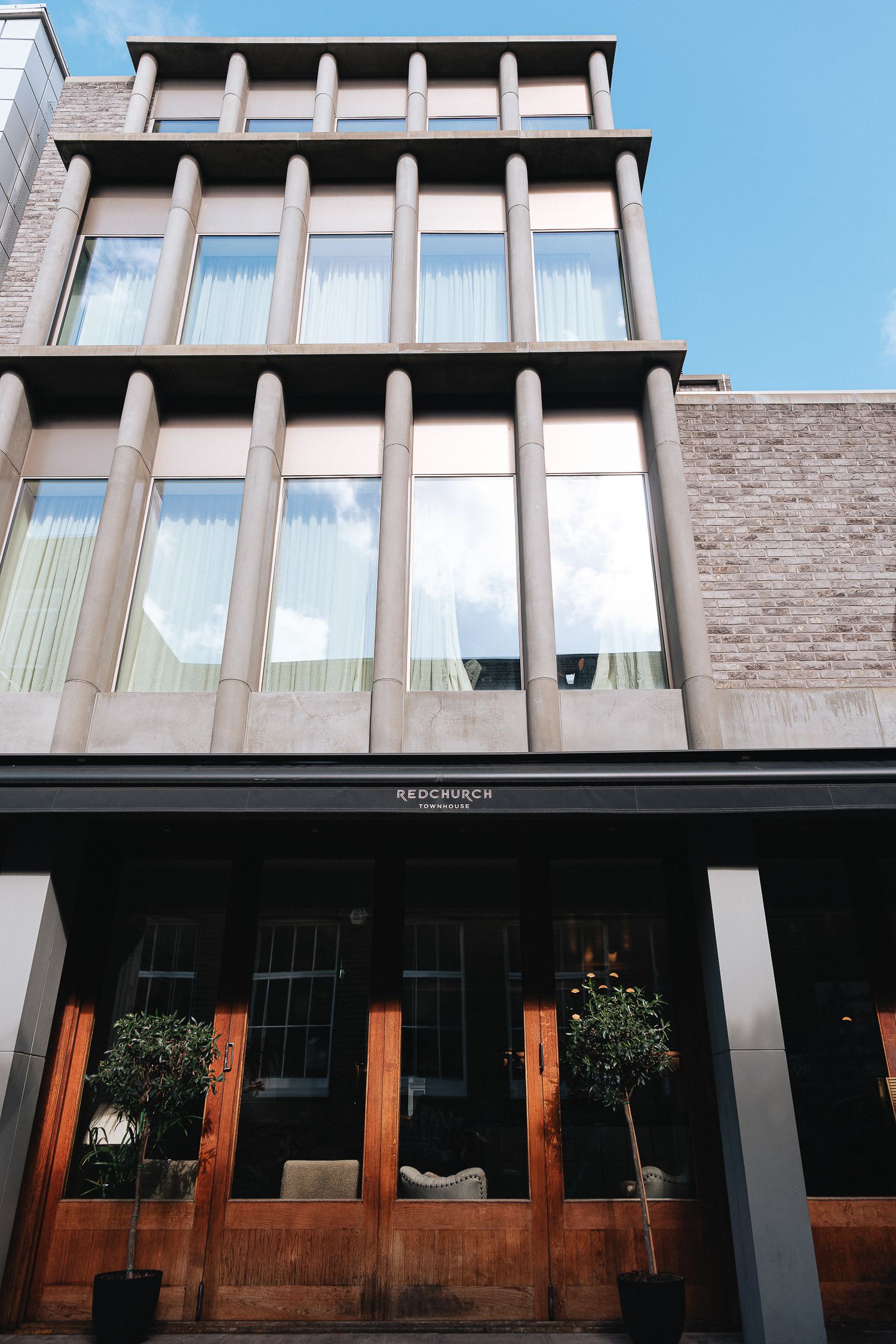 Modern brick building exterior with large windows and wooden accents under blue sky.