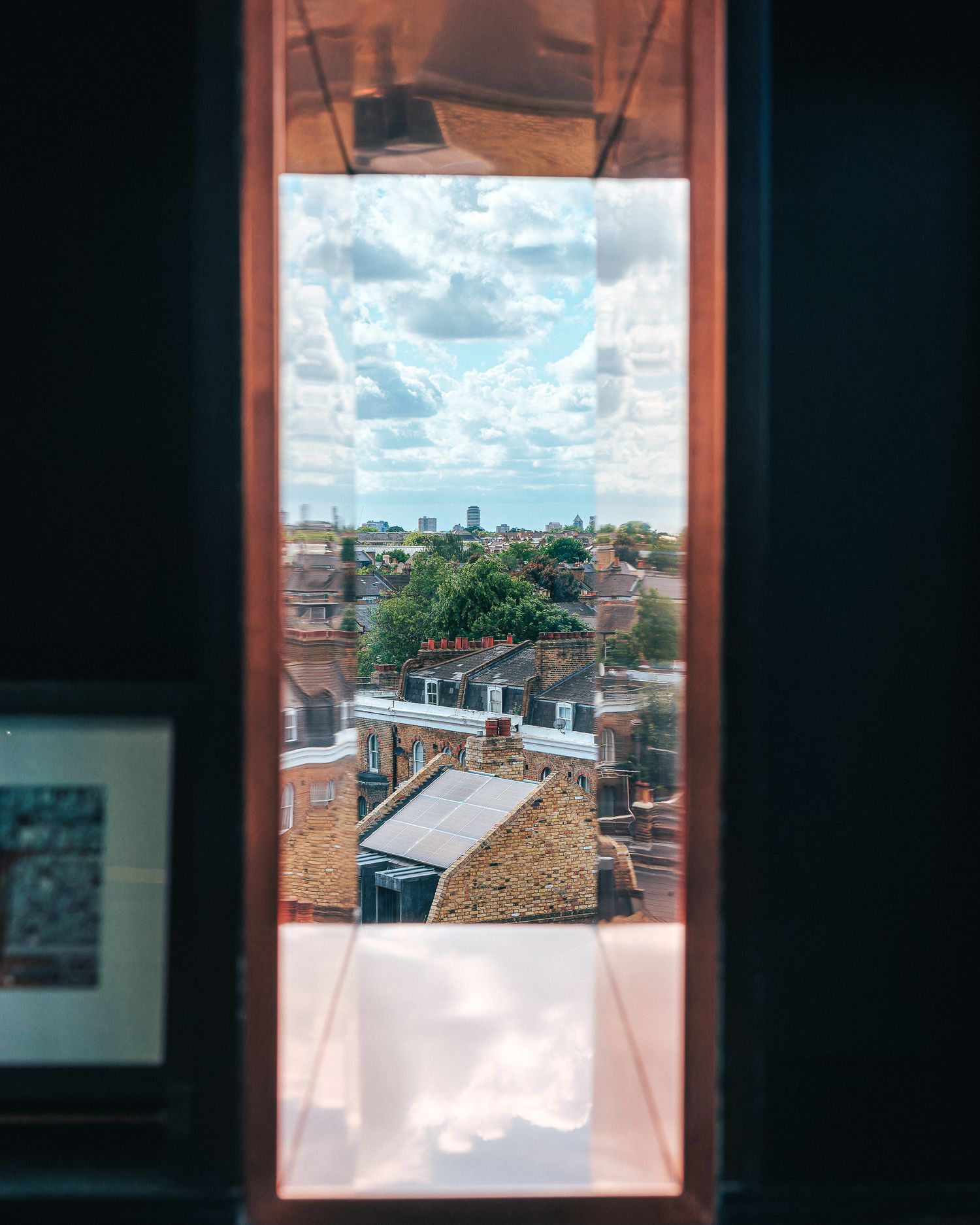 City rooftop view through window frame showing urban architecture and cloudy sky.