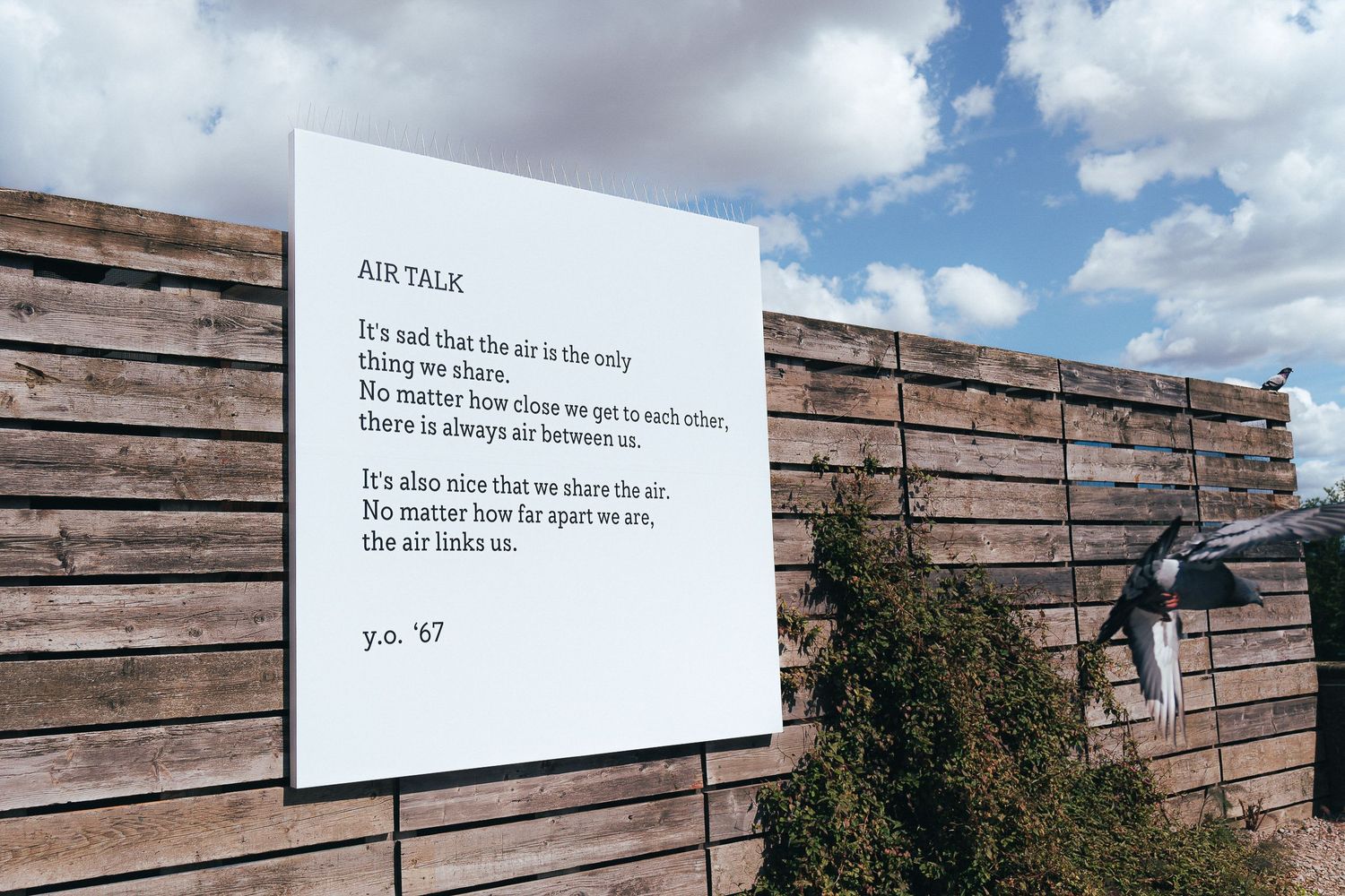 Text installations mounted on wooden wall panels under bright blue sky.