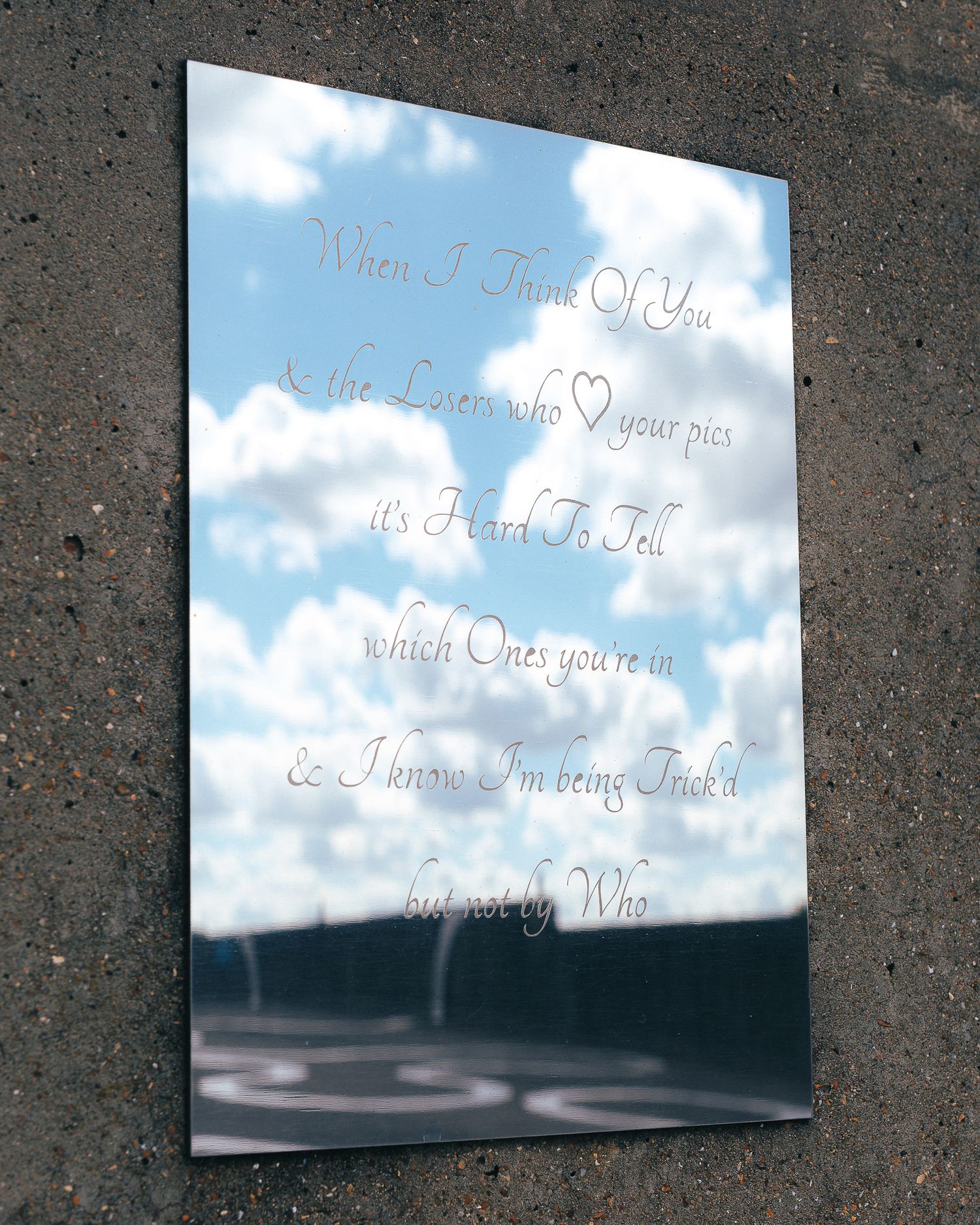 Reflective art installation with text overlaid on mirror surfaces capturing sky and clouds.