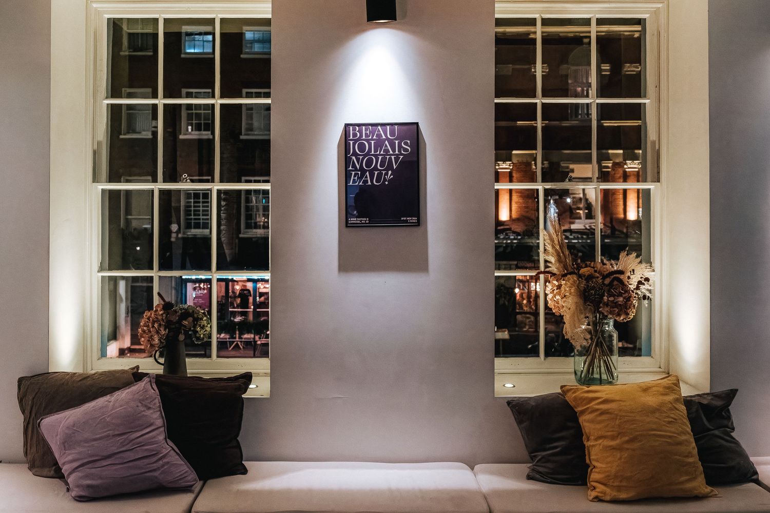 Modern lounge area with white walls, windows, and dark throw pillows arranged on seating.