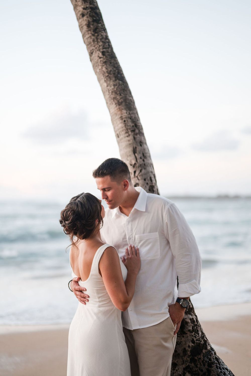 Couple hugging by palm tree during beach engagement session in Puerto Rico