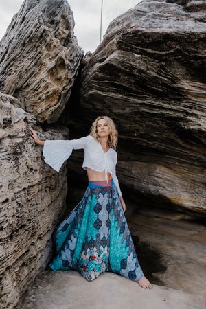 A dramatic pose between large coastal rock formations wearing a blue patterned maxi skirt.