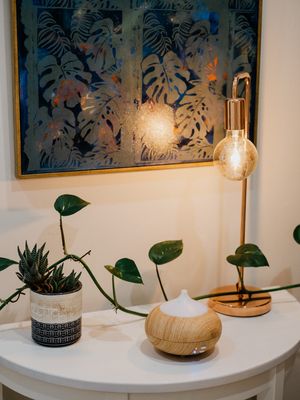 Modern home decor featuring tropical wall art, plants, and a wooden diffuser on white table.