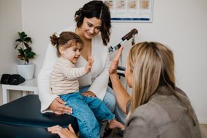 A pediatric medical examination with a smiling toddler and healthcare providers.