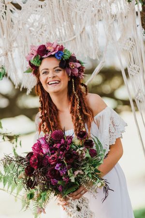 Bridal portraits with vibrant purple flower crown and bouquet under macrame decor.