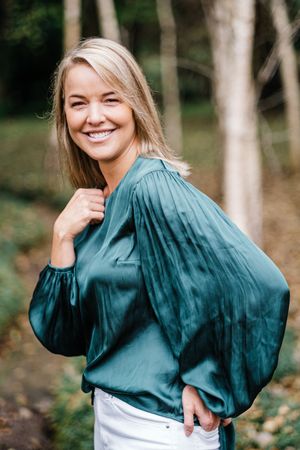 Woman in emerald green satin blouse poses playfully in outdoor setting.