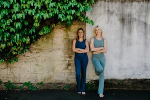 Two people in athletic wear pose against vine-covered wall in urban setting.