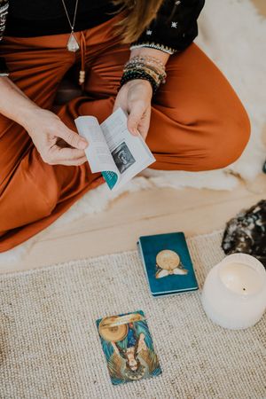 Hands arranging tarot cards and spiritual objects on a textured carpet.