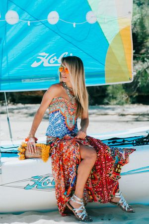 Woman in colorful floral dress posing on beach under blue canopy tent.