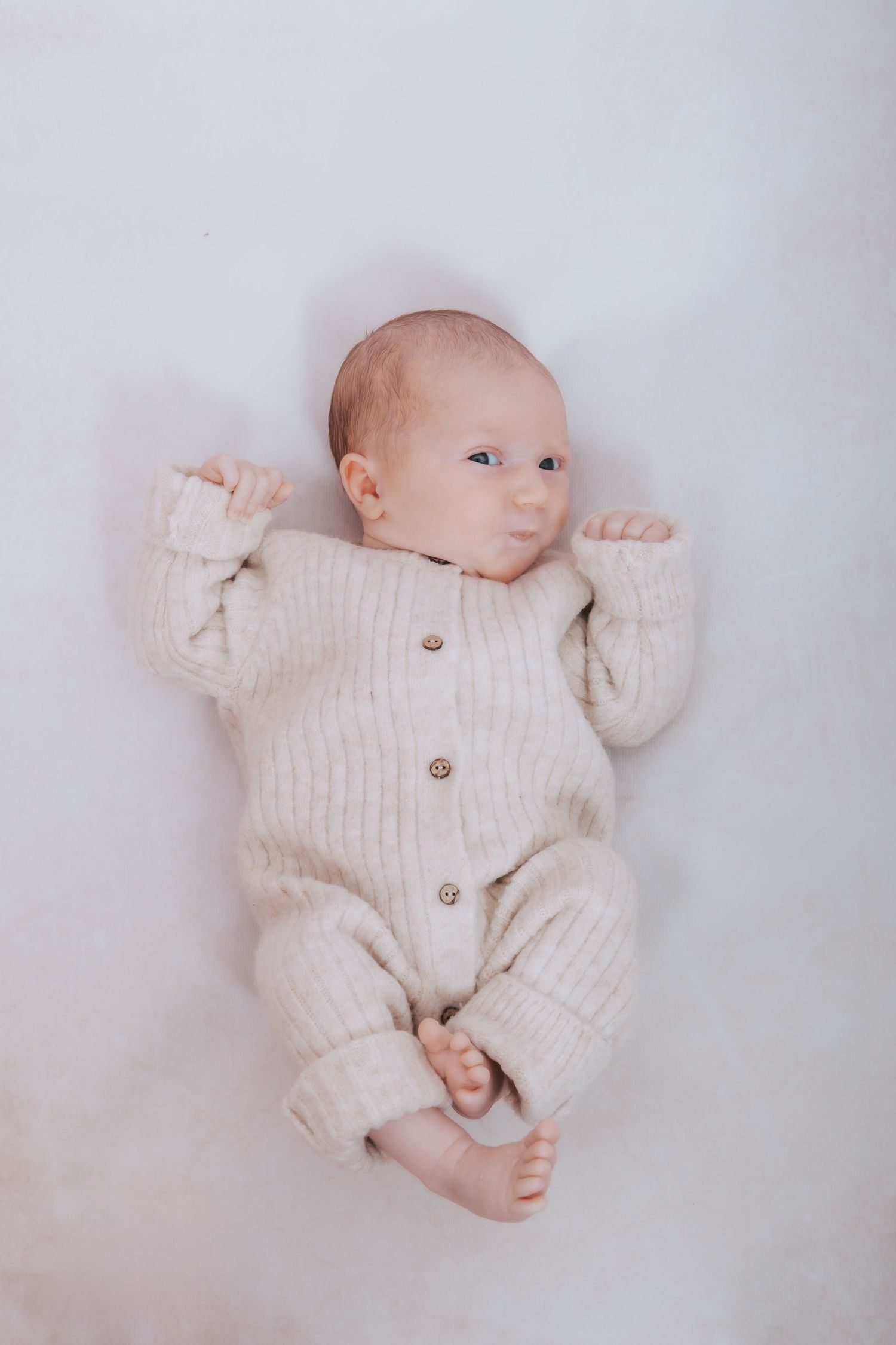 A baby wearing a cream knit romper lying on white fabric in various poses.