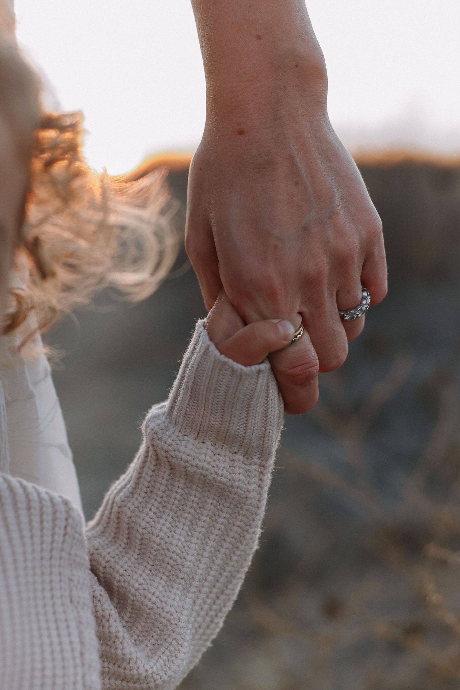 Hand gently holding a white knit sweater sleeve against a blurred outdoor background at sunset for family photoshoot