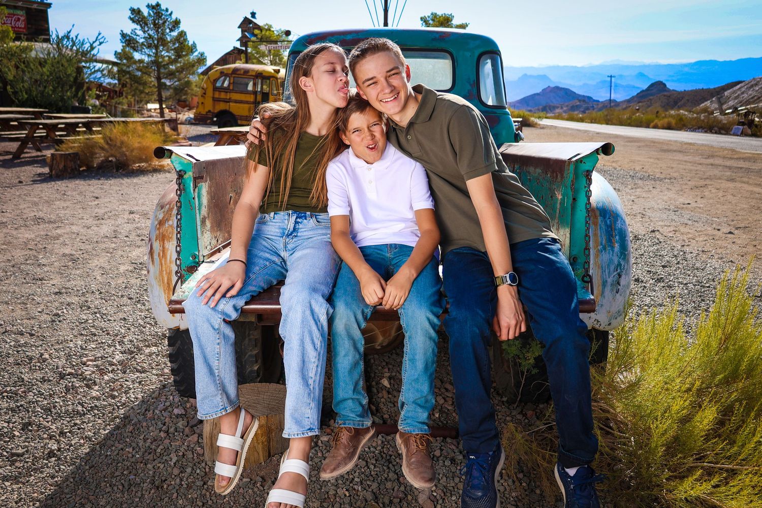 Family sits together on vintage turquoise pickup truck in desert setting.