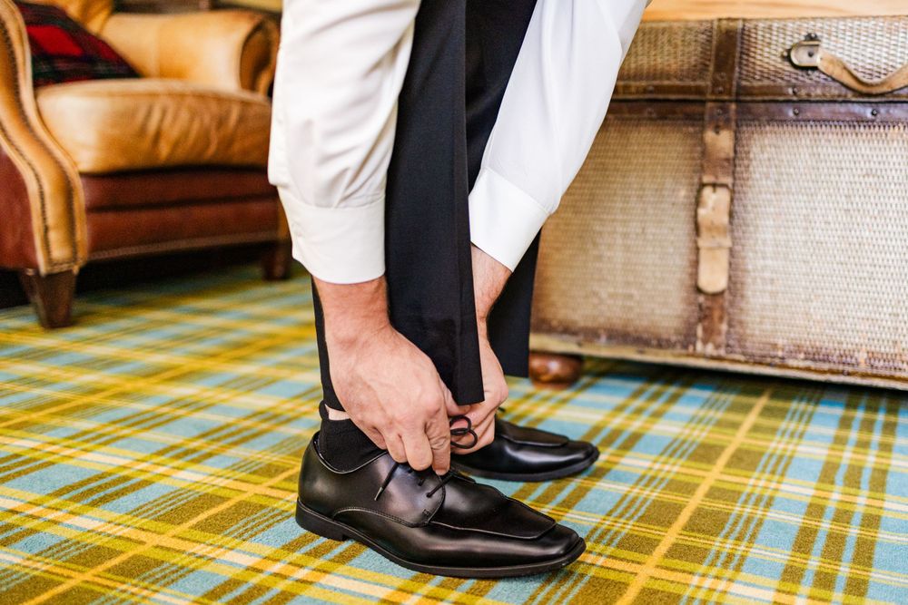 Close-up of groom tying formal black dress shoes on plaid carpet.