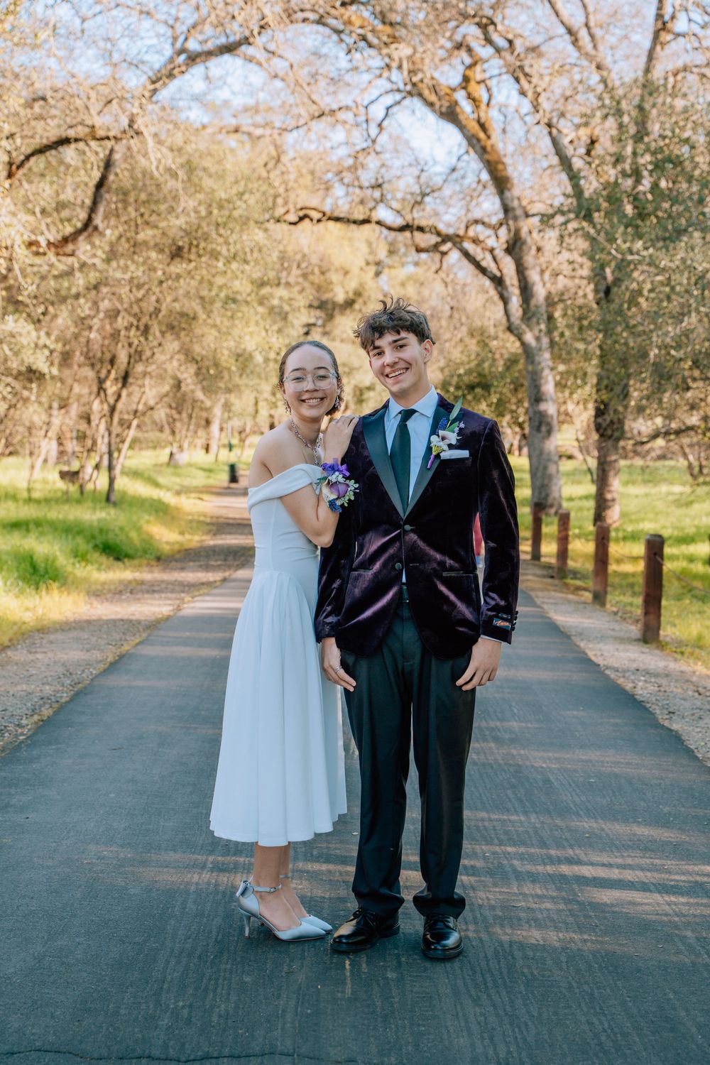 Children in formal attire posing together on paved pathway with trees.