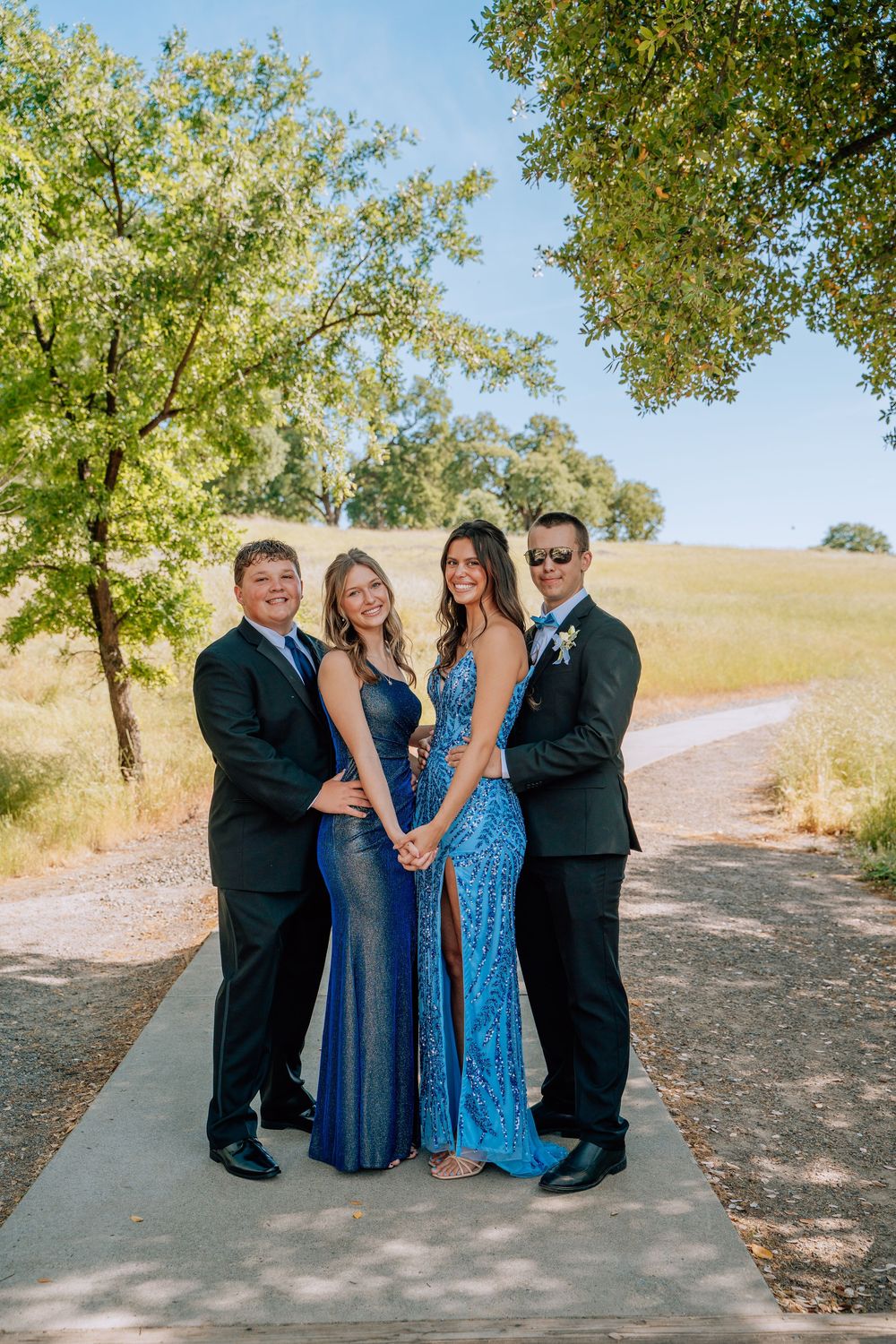 Group photo of people in coordinating blue dresses and dark suits at an outdoor celebration.