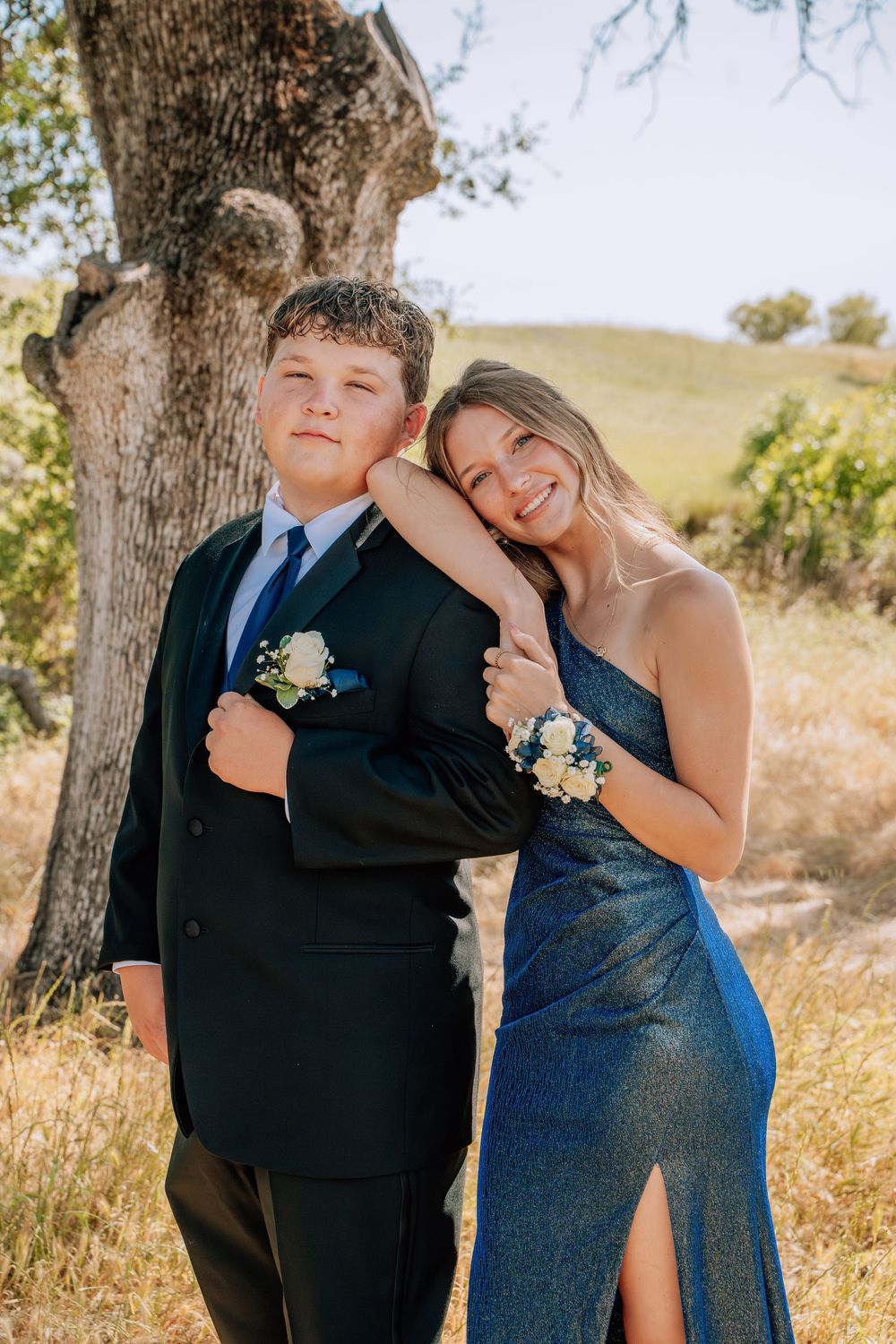 A joyful moment captured between two people in formal wear under a mature tree.