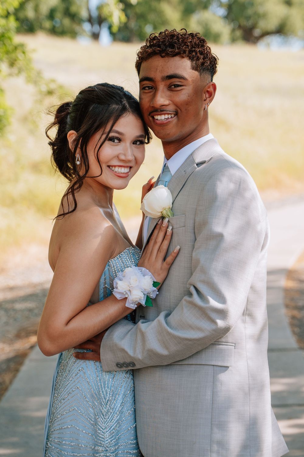 A couple in matching light blue gown and grey suit share an intimate moment outdoors.