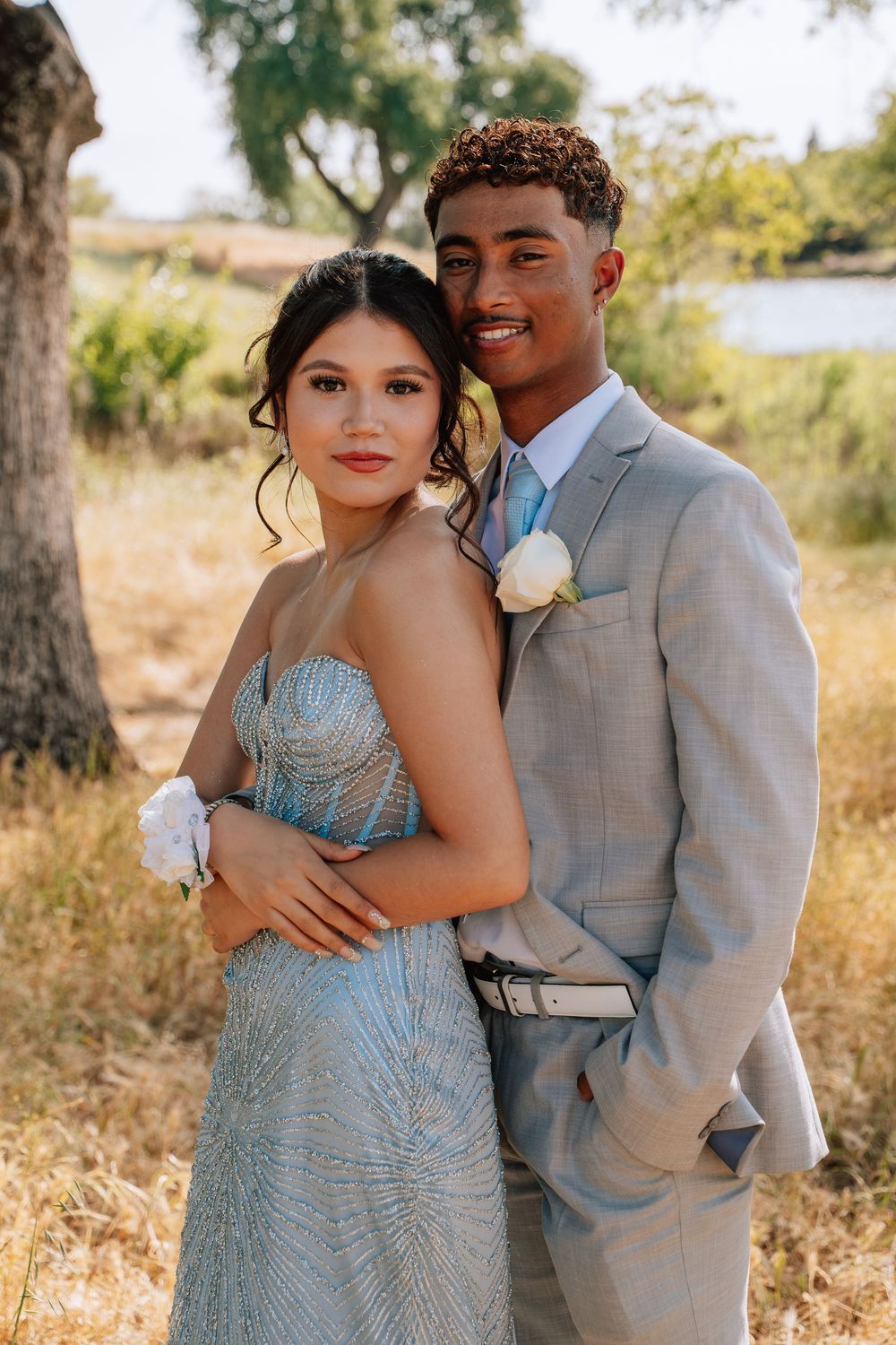 Romantic photoshoot of a couple in blue gown and grey suit against a natural backdrop.