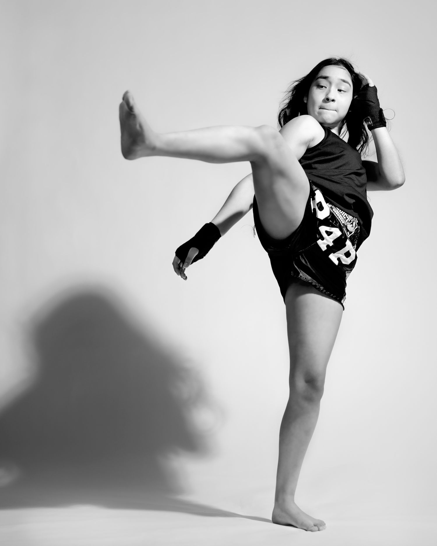 A black and white photo of a martial artist performing a high kick in athletic wear against a plain background.