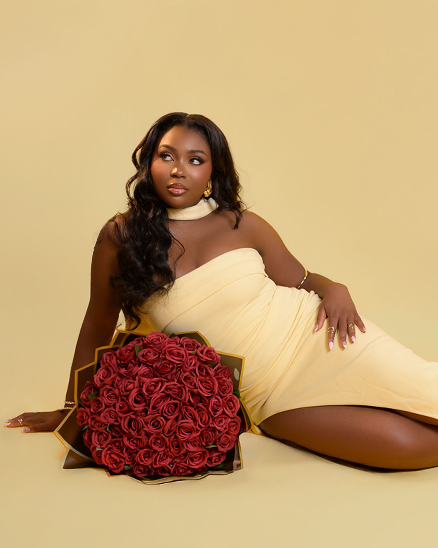 Figure in a black off-shoulder sweater dress sits elegantly in a cream chair while holding a business newspaper.