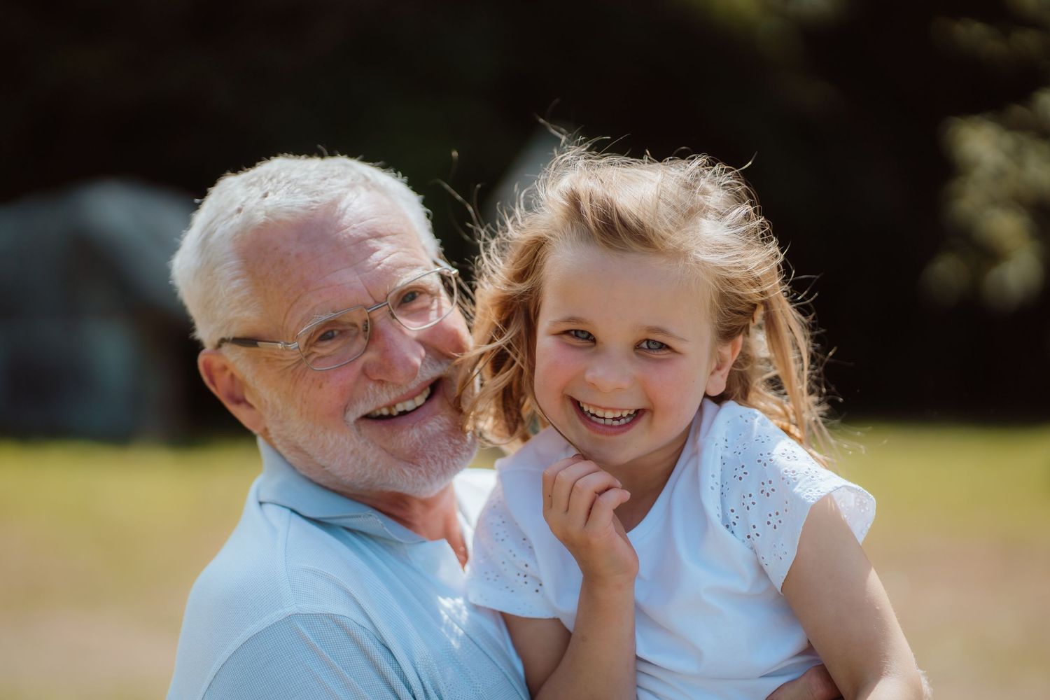 An elderly person and young child share a joyful moment together outdoors on a sunny day.