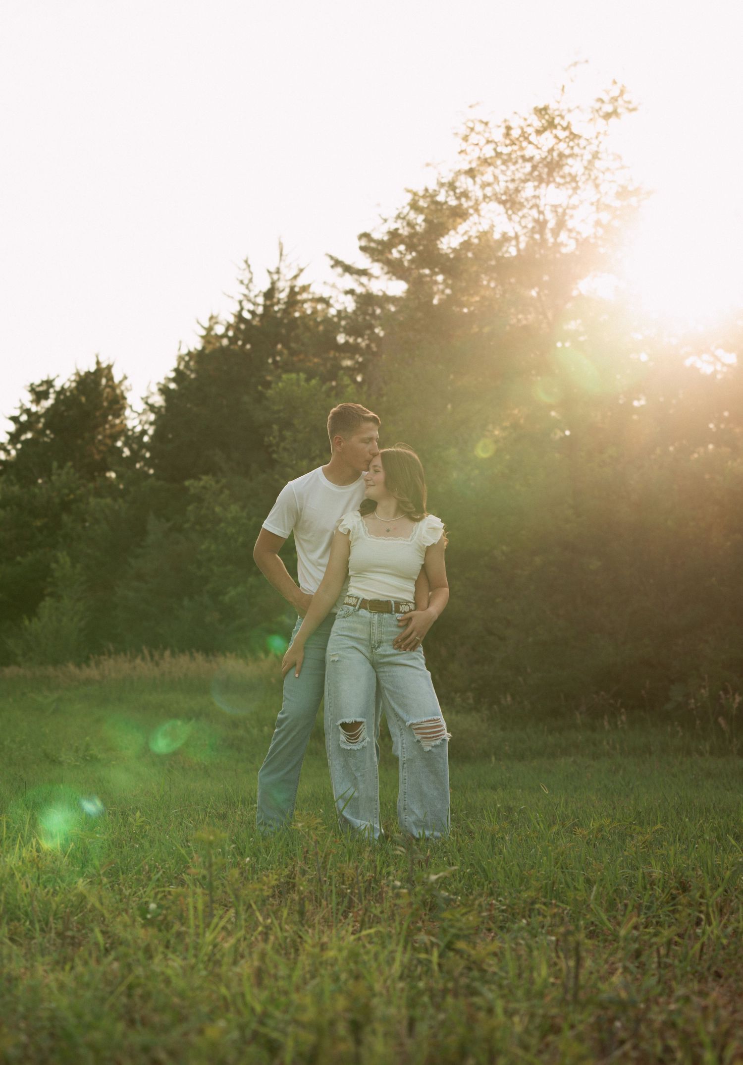 Couple embracing in a sunlit field during golden hour with a dreamy, romantic atmosphere.