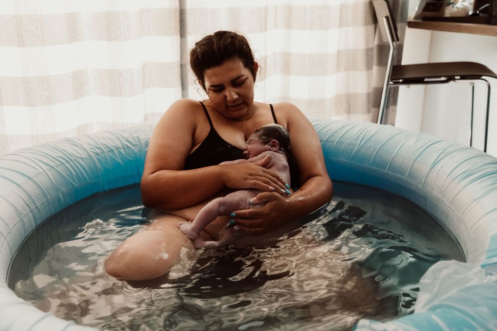 A person relaxes in a blue inflatable birthing pool filled with water during labor.