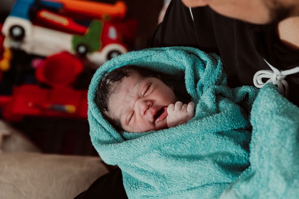 A newborn baby is wrapped in a teal towel after being born in a home water birth setting.